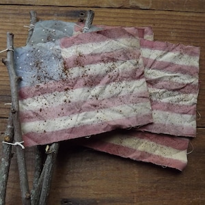 May include: Three weathered American flags tied together with twine, hanging on a wooden surface. The flags are faded and have a rustic look.