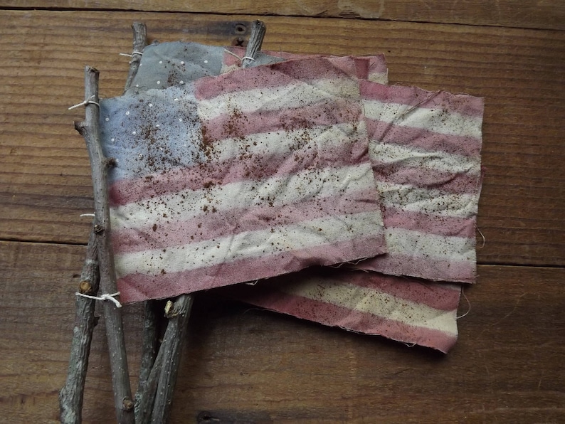May include: Three weathered American flags tied together with twine, hanging on a wooden surface. The flags are faded and have a rustic look.
