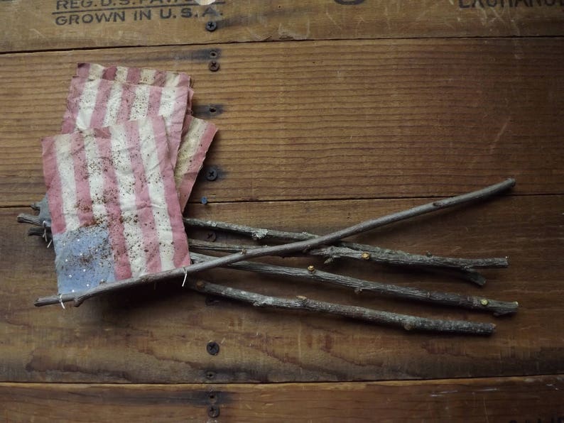 May include: A weathered wooden crate with a small American flag made of fabric and several thin branches laying across the top.