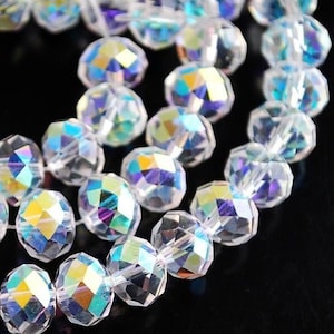 May include: Strands of iridescent, faceted crystal beads. The beads are clear with a rainbow sheen, reflecting colors of blue, green, and yellow. The beads are strung together, creating a shimmering effect. Ideal for jewelry making.