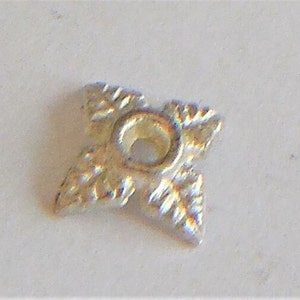 May include: A silver-colored metal star-shaped pendant with a hole in the center. The star has a decorative design with a textured surface.