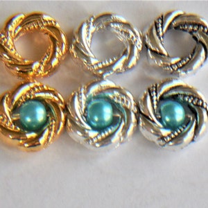 May include: Six decorative metal rings with a twisted design. Three rings are gold and three are silver. The gold rings have a turquoise pearl in the center. The silver rings have a turquoise pearl in the center.