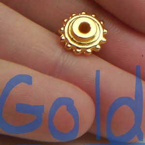 May include: Gold-colored metal bead with a circular design and a small hole in the center.
