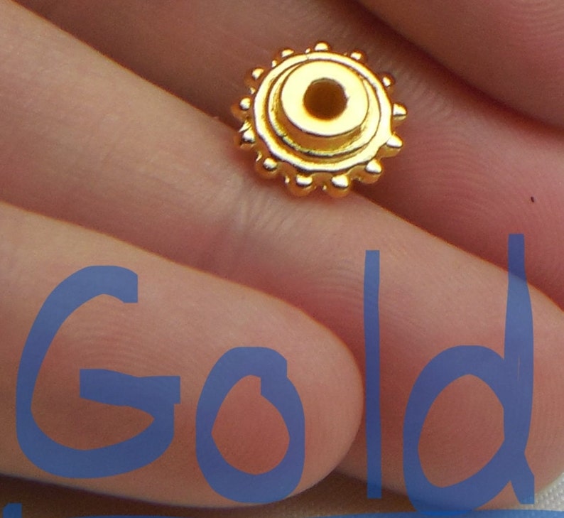 May include: Gold-colored metal bead with a circular design and a small hole in the center.