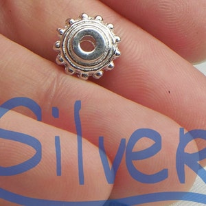 May include: A silver bead with a round, decorative design. The bead has a small hole in the center for stringing.