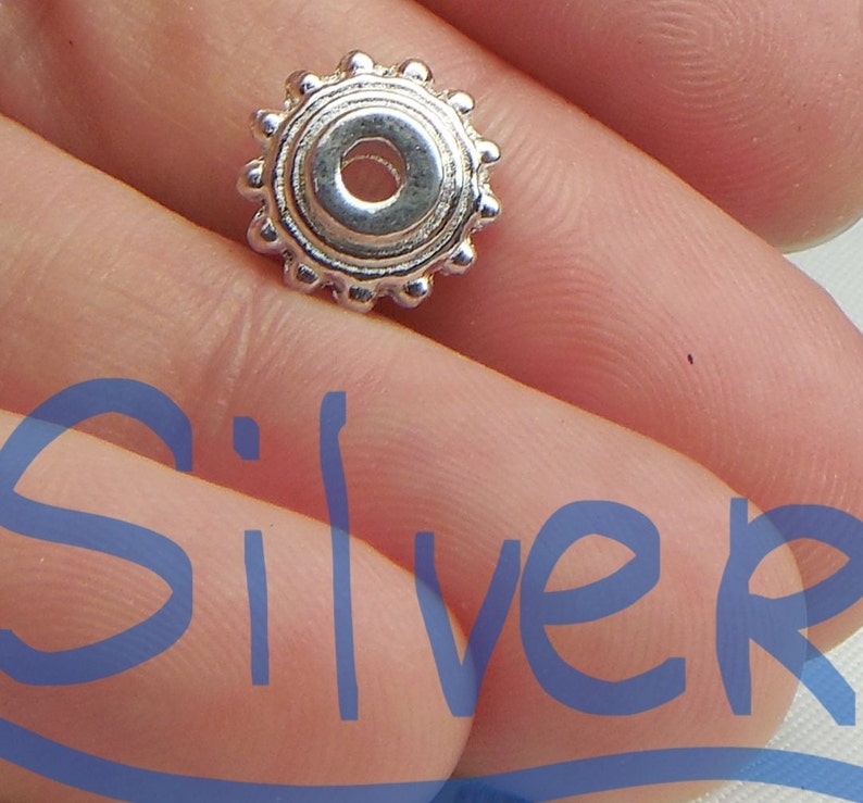 May include: A silver bead with a round, decorative design. The bead has a small hole in the center for stringing.