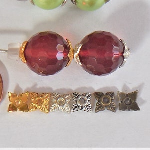 May include: Two dark red faceted glass beads with gold accents and six metal bead caps in gold, silver, and bronze.