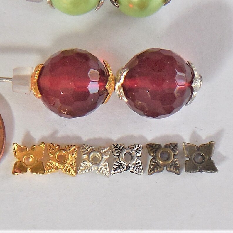 May include: Two dark red faceted glass beads with gold accents and six metal bead caps in gold, silver, and bronze.