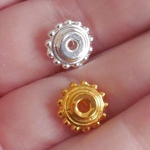 May include: Two round metal beads, one silver and one gold, with a raised circular design and a hole in the center.