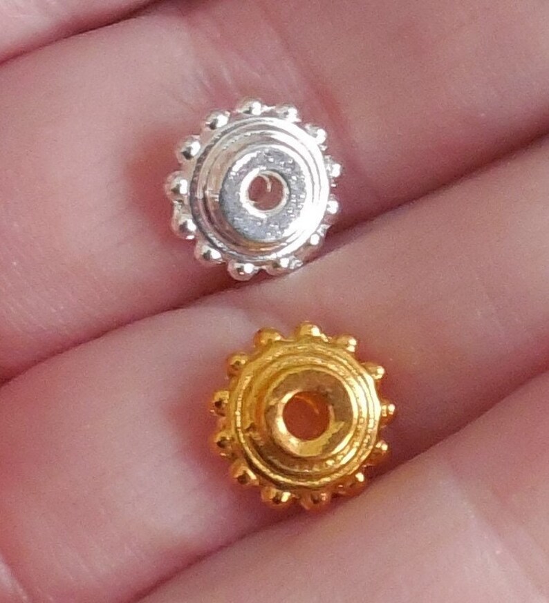 May include: Two round metal beads, one silver and one gold, with a raised circular design and a hole in the center.