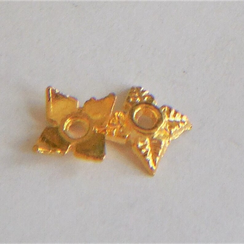 May include: Two gold-colored metal star-shaped beads with a hole in the center. The beads have a decorative design.