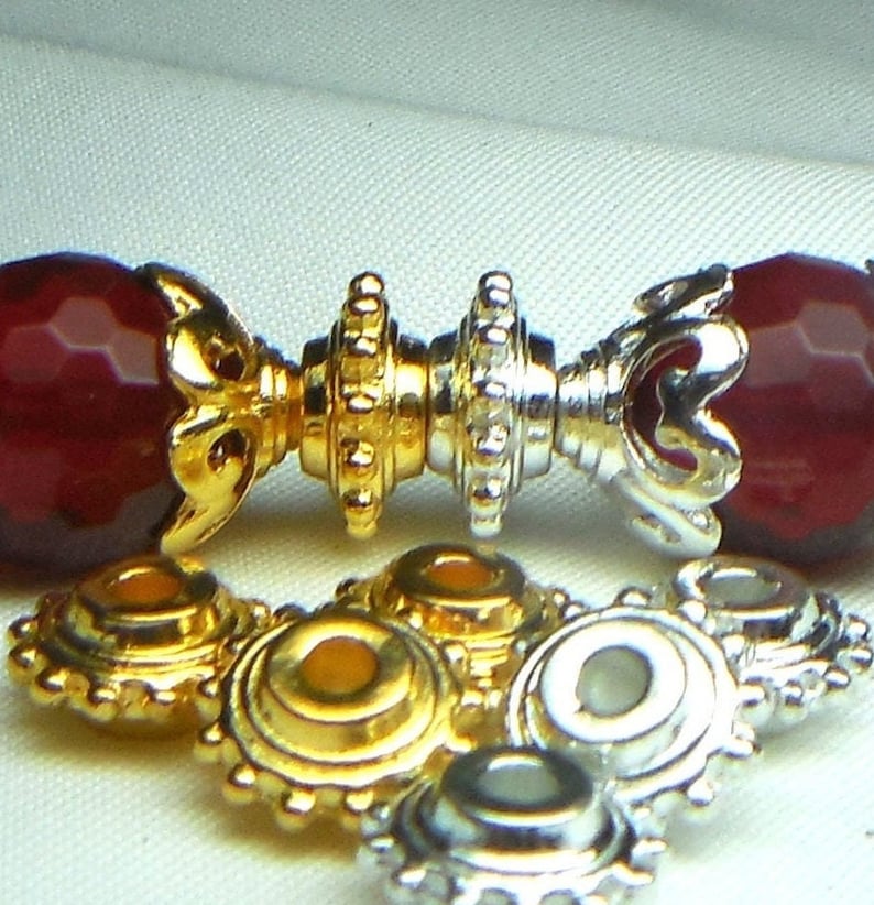 May include: Close-up of gold and silver metal bead caps with a decorative design. The caps are used for jewelry making and crafting.