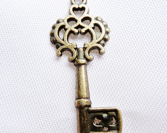 May include: An ornate antique-style key charm made of metal with a gold finish. The key has a decorative head with intricate swirls and a heart-shaped design. The key is about 2 inches long.