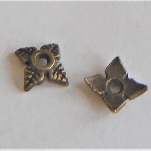 May include: Two antique gold-toned metal star-shaped embellishments with a hole in the center. The embellishments have a decorative design of leaves around the edges.