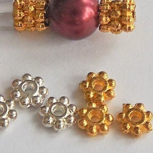 May include: A close-up of six metal bead caps. Three are silver and three are gold. Each cap has a flower-like design with a small hole in the center.