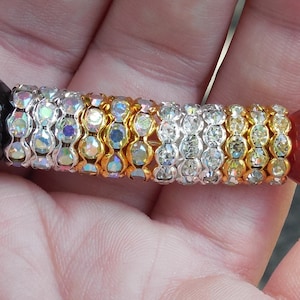 Op de afbeelding: Een close-up van een veelkleurige kralenarmband met zwarte, gouden, zilveren en rode kralen. De armband is gemaakt van kleine, ronde kralen die aan elkaar geregen zijn op een dun koord.