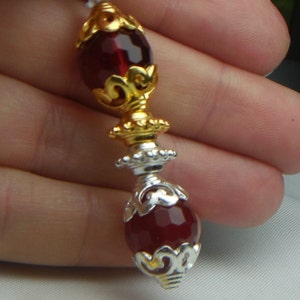 May include: A close-up of a red glass bead with gold and silver filigree accents. The bead is round and has a shiny finish.