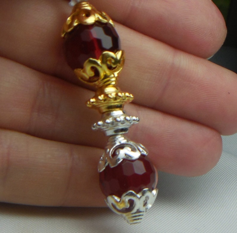 May include: A close-up of a red glass bead with gold and silver filigree accents. The bead is round and has a shiny finish.