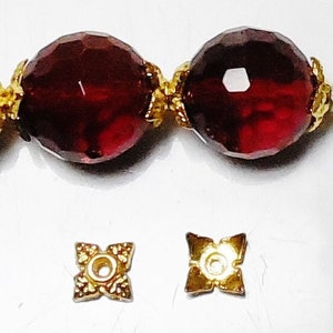 May include: Two red faceted glass beads with gold metal connectors and two gold metal bead caps with a star-shaped design.