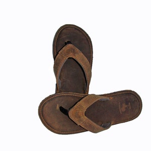 以下が含まれることがあります： 茶色の革製のビーチサンダルで、茶色の革のストラップと茶色の革のソールが付いています。