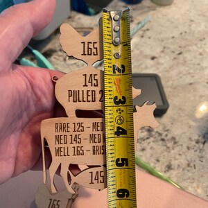 May include: Wooden cutouts of a chicken, cow, and fish with different internal temperatures listed for different levels of doneness. The cutouts are measured with a yellow tape measure.