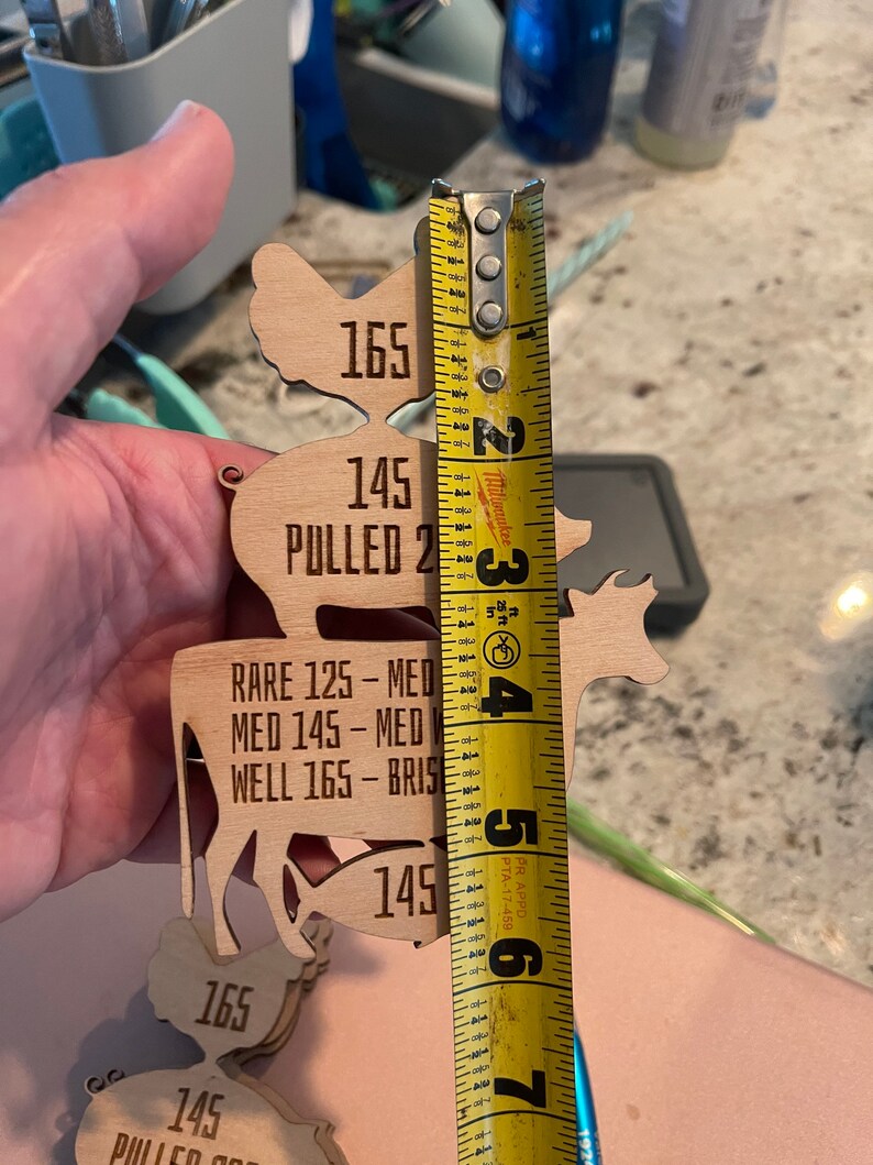 May include: Wooden cutouts of a chicken, cow, and fish with different internal temperatures listed for different levels of doneness. The cutouts are measured with a yellow tape measure.