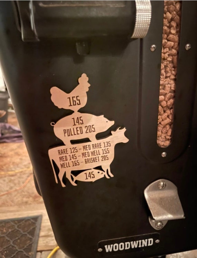 May include: A black metal smoker with a woodwind logo and a brown wood pellet hopper. A metal sticker with a chicken, pig, cow, and fish silhouette shows recommended cooking temperatures for different meats. The sticker reads "165", "145", "PULLED 205", "RARE 125 - MED RARE 135", "MED 145 - MED WELL 155", "WELL 165 - BRISKET 205", and "145".