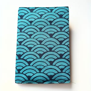 May include: A rectangular, fabric-covered item with a repeating pattern of teal and navy blue fan-like shapes. The item is likely a case or cover, possibly for a book or electronic device. The fabric has a textured appearance.