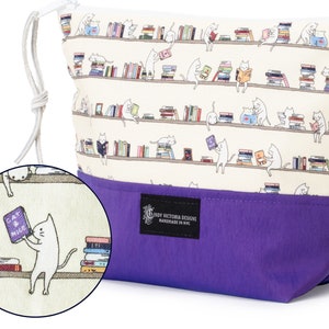 May include: A purple and cream drawstring pouch with a repeating pattern of cats reading books on shelves. The pouch has a label that reads "Cindy Victoria Designs Handmade in NYC".