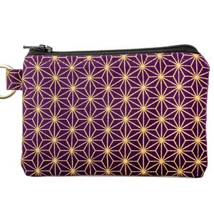 May include: A small purple zippered pouch with a gold geometric pattern. The pouch has a ring attached to the side.