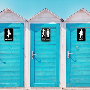 Puede incluir: Tres puertas de madera azul con moldura blanca. Cada puerta tiene un letrero negro con una silueta blanca de una sirena, una sirena y un pirata, y un pirata. Los letreros dicen "Mujeres", "Aseo" y "Hombres".