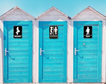 May include: Three blue wooden doors with white trim. Each door has a black sign with a white silhouette of a mermaid, a mermaid and a pirate, and a pirate. The signs read "Women", "Restroom", and "Men".
