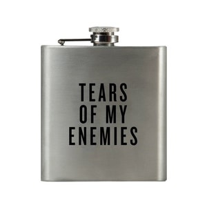 May include: A silver flask with a black inscription that reads "Tears of my Enemies".
