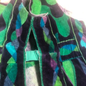 May include: Close-up of a green, blue, and purple velvet fabric with a geometric pattern. The fabric has a zipper on the side.