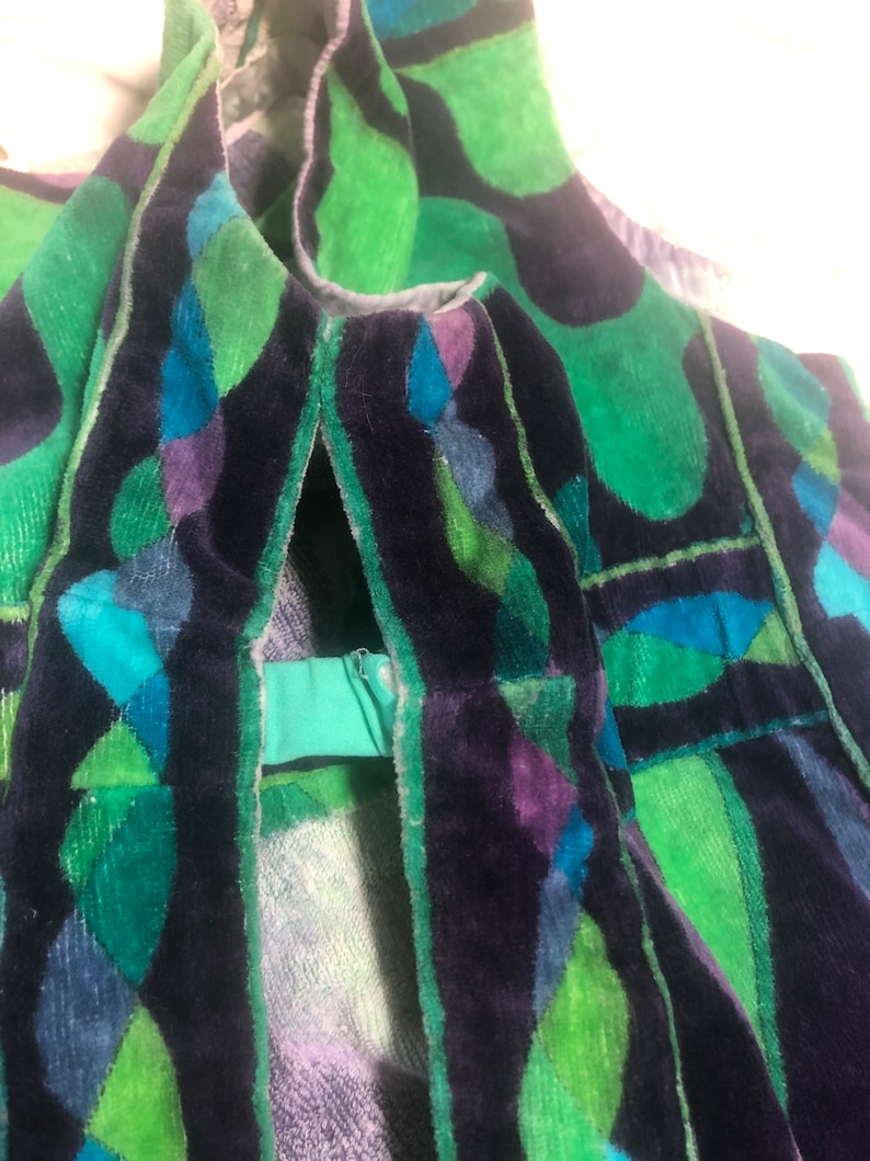 May include: Close-up of a green, blue, and purple velvet fabric with a geometric pattern. The fabric has a zipper on the side.