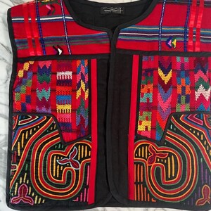 May include: A red and black waistcoat with colourful embroidery. The waistcoat has a black fabric base with red trim and a variety of colourful geometric patterns stitched on the front.