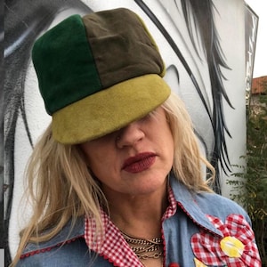 May include: A green, brown, and yellow patchwork cap with a wide brim. The cap is made of a soft, textured fabric.
