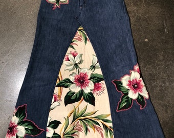 May include: A long denim skirt with a floral print panel. The skirt has a high waist and a flared silhouette. The floral print is in shades of pink, white, and green.