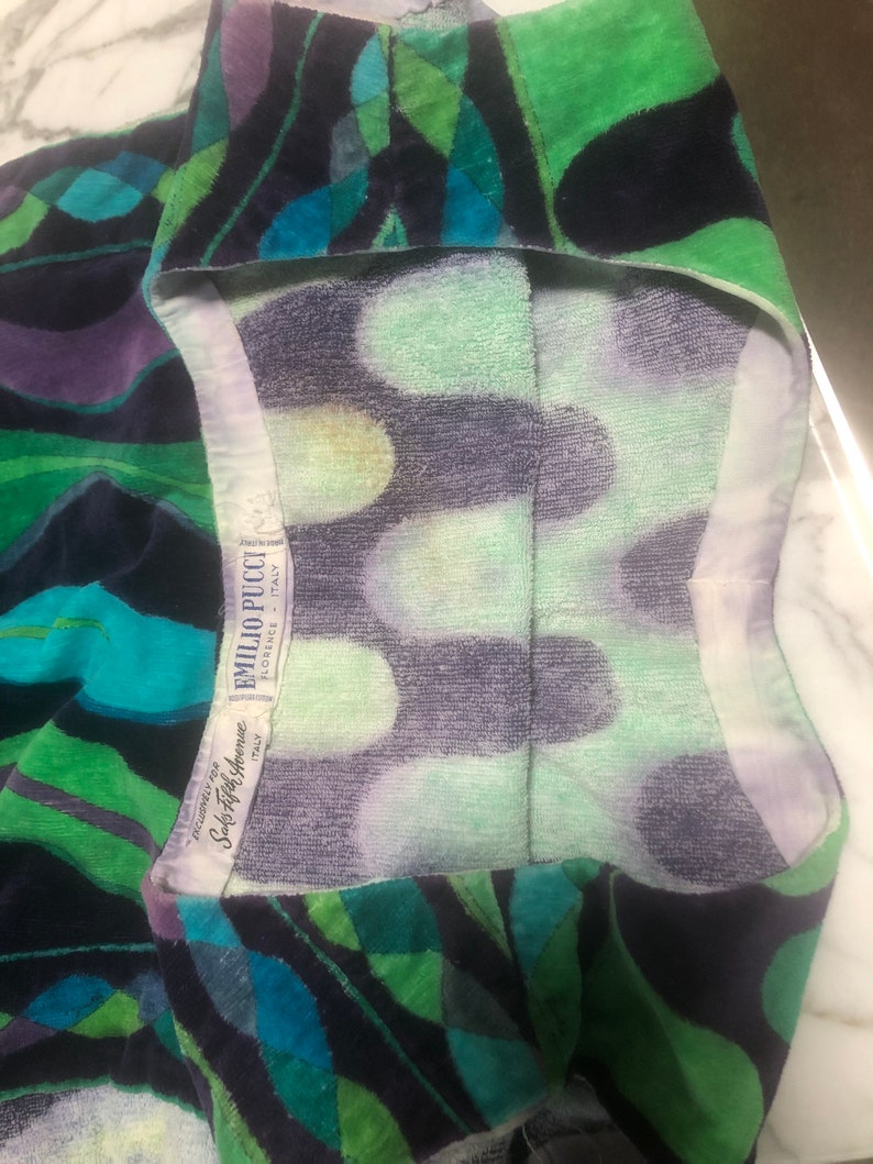 May include: A green, blue, and purple patterned towel with a white label that reads "Emilio Pucci, Made in Italy,  Sole Agent for America, Saks Fifth Avenue".