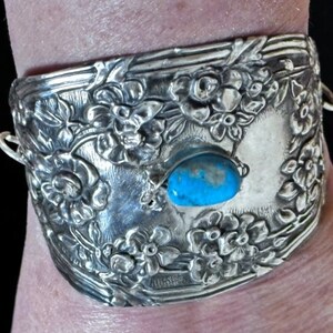 May include: A silver bracelet with a floral design and a turquoise stone. The bracelet is made of metal and has a detailed design.