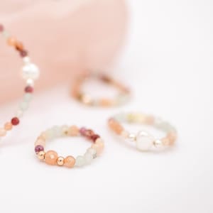 May include: Three beaded rings with a mix of pink, green, and brown beads. One ring has a white pearl bead.