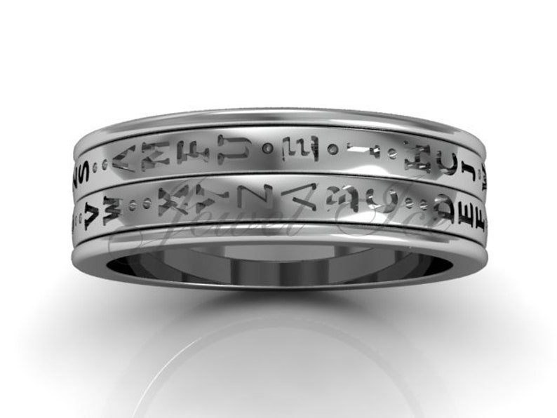 May include: A silver band with three rows of engraved text. The text is in a stylised font and appears to be a language other than English.