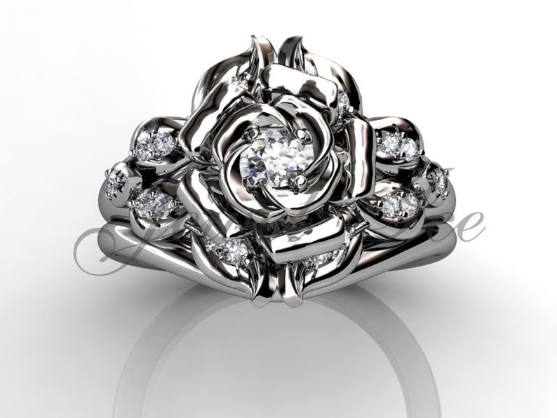 Puede incluir: Un anillo de compromiso de plata en forma de rosa con un gran diamante central y diamantes m&aacute;s peque&ntilde;os engastados en los p&eacute;talos. El anillo est&aacute; dise&ntilde;ado para ser usado con una banda de boda a juego.