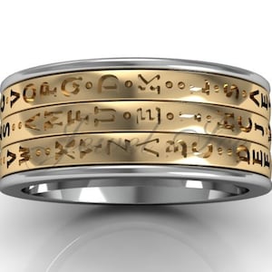 May include: A silver and gold band ring with a repeating pattern of symbols around the band.