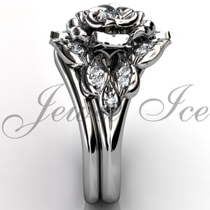 Puede incluir: Un anillo de compromiso de oro blanco en forma de rosa con un solo diamante en el centro de la rosa y diamantes m&aacute;s peque&ntilde;os en las hojas. El anillo est&aacute; sobre un fondo blanco.