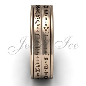 May include: A gold-coloured spinning band ring with the alphabet engraved around the band.