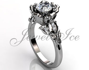 Peut inclure: Une bague de fiançailles en argent en forme de rose avec une grosse pierre centrale transparente et de petites pierres d'accent sur la bande. La bague est posée sur un fond blanc.
