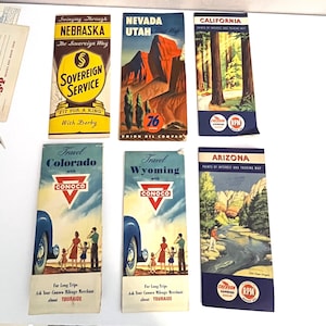 May include: A collection of vintage travel brochures featuring state maps and scenic illustrations. Brochures include "Nebraska," "Nevada," "California," "Colorado," "Wyoming," and "Arizona." The brochures showcase classic designs and text, including "Sovereign Service" and "Conoco."