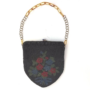 May include: A black beaded handbag with a floral design in red, blue, and green. The purse has a tortoiseshell chain handle and a clasp closure. The bag is shield-shaped.