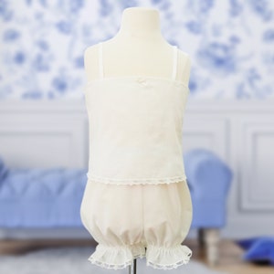 Puede incluir: Un conjunto de bombachos para bebé de algodón blanco con ribete de encaje. El conjunto incluye una camiseta sin mangas y bombachos.